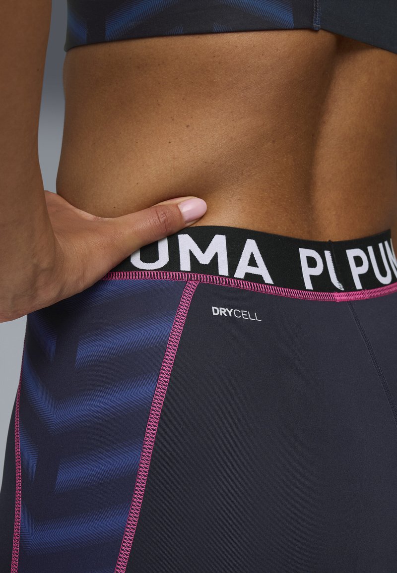 Fascia elastica nera con logo "PUMA", tessuto grigio scuro con motivo a freccia blu, dettaglio di cucitura rosa, etichettato "DRYCELL".