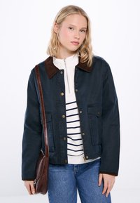 Mörkblå jacka med brun manchesterkrage, knäppning fram, två framfickor, tillsammans med en vit zip-up skjorta och randig topp.