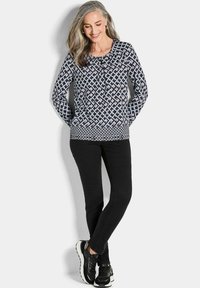 Langärmliges, marineblaues Oberteil mit einem geometrischen Muster in Helllila und Weiß. Kombiniert mit schwarzen Slim-Fit-Hosen und schwarzen Sneakern.