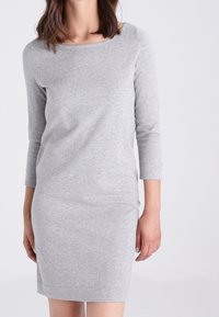 Robe gris ajustée en tissu doux, dotée d'un col bateau et de manches trois-quarts. Texture lisse sans motifs ni accents visibles.