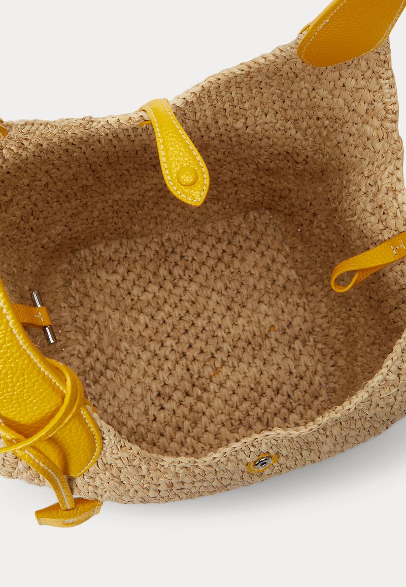 Sac cabas en paille tissée avec poignées en cuir jaune, fermeture à bouton-pression et bouton à pression, vu de l'intérieur.