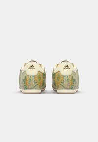 Zelené tenisky Adidas s květinovým vzorem a krémovými akcenty, zdobené žlutými a fialovými květinami, gumovou podrážkou a logem na patě.