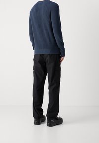 Pull en maille bleu marine avec ourlet et poignets côtelés, porté avec un pantalon cargo noir doté de poches latérales et des baskets noires.