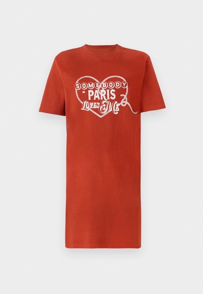Red cotton t-shirt with short sleeves, featuring a white heart graphic and text reading "Somebody in Paris Loves Me." Smooth texture.