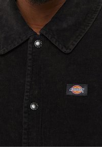 Czarna koszula z korduroju z zapięciem na guziki, z dużym kołnierzem i małą naszywką logo Dickies po lewej stronie.