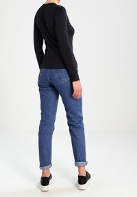 Czarna bluzka z długim rękawem w połączeniu z niebieskimi, wysokim stanem jeansami z mankietami oraz czarnymi butami wsuwanymi. Prosty, dopasowany fason.