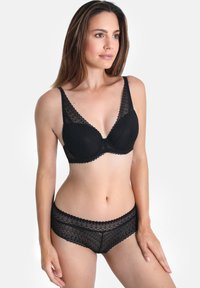 Schwarzer Spitzen-BH mit einem tiefen Ausschnitt und gewellten Kanten, kombiniert mit passenden Spitzen-Boyshorts, die ein ähnliches gewelltes Design aufweisen.