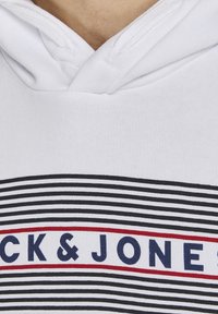 Sweat à capuche blanc avec des rayures horizontales noires et un logo rectangulaire bordé de rouge affichant le texte bleu marine « CK & JONES ».