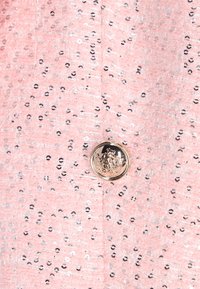 Tessuto rosa con paillettes caratterizzato da una superficie strutturata, impreziosito da un bottone rotondo tono oro con design a corona.