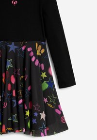 Schwarzes Langarmkleid mit einem einfarbigen Oberteil und einem Faltenrock, der mit bunten Stern- und Wirbelmustern in Rosa, Blau, Gelb und Grün verziert ist.