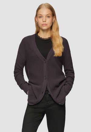 Cardigan violet foncé en tricot texturé avec un col en V, des boutons sur le devant et des poignets côtelés, porté sur un haut noir et assorti avec un pantalon noir.
