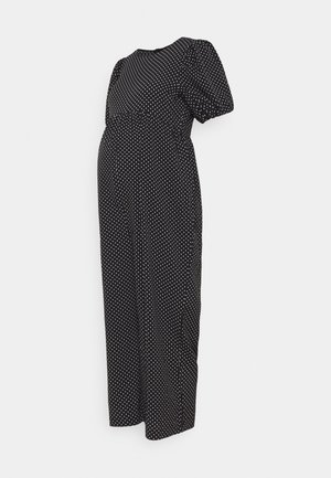 Robe de maternité noire à pois blancs, manches courtes bouffantes et taille empire, présentée sur un fond uni.