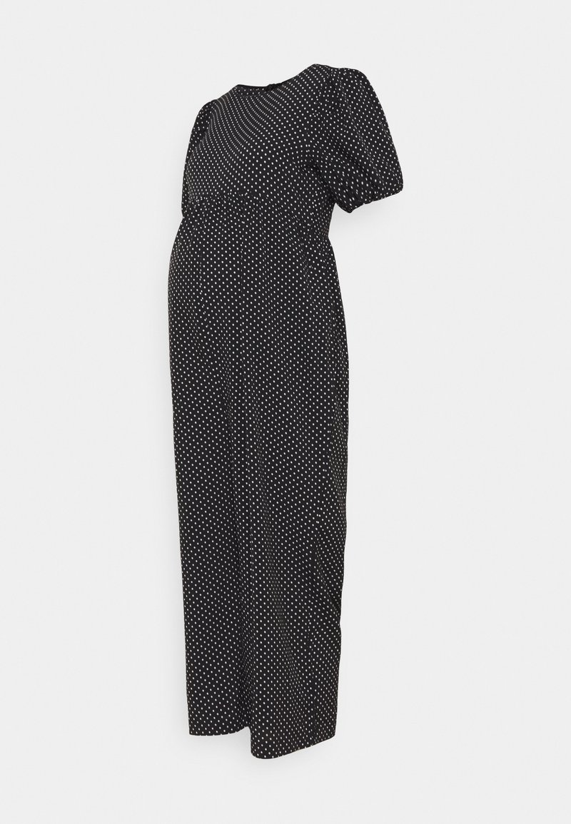 Robe de maternité noire à pois blancs, manches courtes bouffantes et taille empire, présentée sur un fond uni.