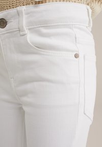 Vita denimjeans med en mjuk textur, med framfickor och en liten metallknapp som accent vid midjan.