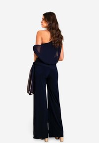 Salopette navy à jambes larges, avec un wrap transparent et un design décolleté, fabriquée à partir d'un tissu doux et fluide.