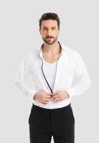 White long-sleeve shirt with contrasting navy accents, button-down front, and soft fabric. Worn over a white V-neck undershirt.