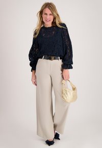 Marineblauw kanten top met pofmouwen, beige wijde broek met hoge taille, zwarte riem en kleine gouden metallic handtas.