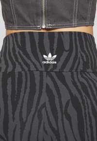 Svart- och grårandiga leggings med zebramönster, tillverkade av stretchig allt, med en broderad vit Adidas-logotyp på midjan.