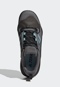 Männlicher Wanderschuh mit einem grauen Mesh-Obermaterial, türkisfarbenen Akzenten und schwarzer Gummisohle. Verfügt über ein Schnürsystem und einen gepolsterten Knöchelbereich für zusätzlichen Komfort.