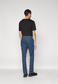Un pantalon en coton bleu présente un design à jambe droite avec des poches à l'arrière et une taille sécurisée. Associé à une chemise noire à manches courtes.