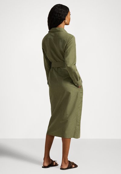 Dolga olivno zelena srajčna obleka z pasom v pasu, dolgimi rokavi in stranskimi žepi. Izdelana iz teksturirane tkanine, z ovratnikom in gumbi na manšetah.