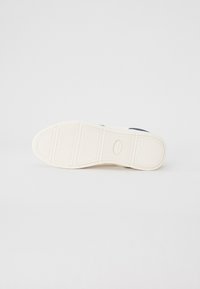 White sneaker sole with textured patterns; rubber material; features oval logo and defined grip lines in various segments.