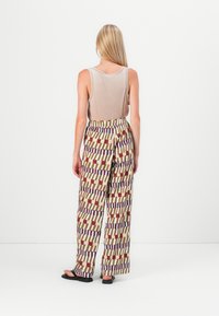 Canottiera beige chiaro abbinata a pantaloni larghi con un audace motivo geometrico in rosso, marrone e blu su uno sfondo crema.