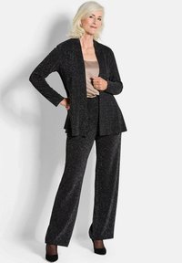 Zwarte pak met een lange open blazer en wijde broeken, accenten met een subtiele glans. Binnenste top van zachte beige satijn.