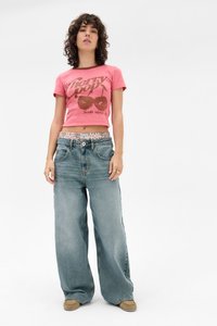 Rosa cropped T-Shirt mit Kirschenmotiv; hellblaue weit geschnittene Jeans mit gemustertem Bund; helle Schuhe mit gesteppten Akzenten.