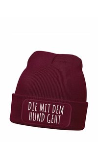 Burgundy knit beanie with a textured design and a cuff. Features a rectangular patch with white text: "DIE MIT DEM HUND GEHT."