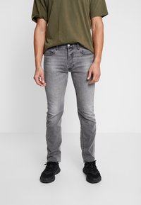 Grå slim-fit jeans med blekt tvätt, med fem fickor och knappstängning. Matchat med en olivgrön t-shirt och svarta sneakers.