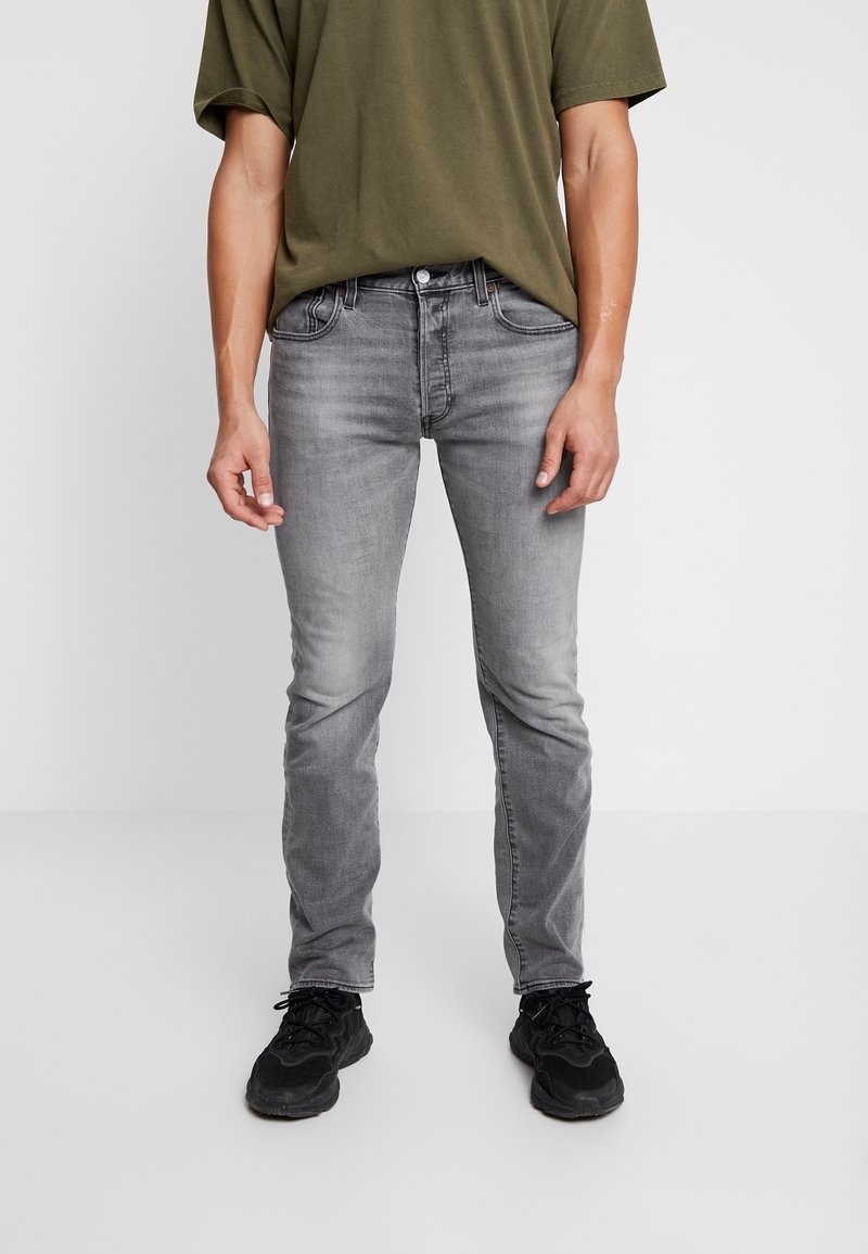 Grå slim-fit jeans med blekt tvätt, med fem fickor och knappstängning. Matchat med en olivgrön t-shirt och svarta sneakers.