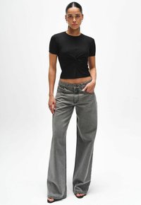 Zwarte getailleerde top met korte mouwen en een twistdetail in het midden, gecombineerd met hoge taille grijze wijde jeans. Soepele textuur, casual ontwerp.