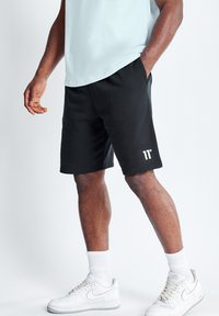 Pantalones cortos deportivos negros con cintura elástica y detalle de logo, combinados con una camiseta azul clara y zapatillas blancas con suela texturizada.