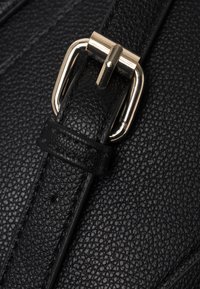 Correa de bolso de cuero texturizado negro con un buckl de metal tono dorado, que presenta una superficie de grano y detalles en el extremo de la correa.
