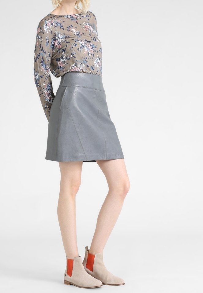 Falda A de piel gris combinada con una blusa de manga larga con estampado floral y botas de tobillo beige con acentos naranjas en los laterales.