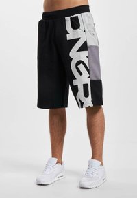 Black and gray athletic shorts with large white text, elastic waistband, and side pockets. Made from a soft fabric with color-blocking design.