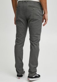 Pantaloni in cotone grigi con vestibilità slim, dotati di due tasche posteriori con cuciture orizzontali e dettagli in bottone. Abbinati a sneaker nere.