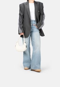 Blazer gris à rayures fines avec des rayures noir et blanc sur les manches, t-shirt blanc, jeans large bleu clair et sac à bandoulière beige.