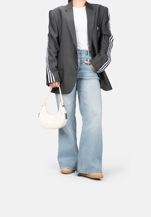 Blazer grigio a righe con strisce bianche e nere sulle maniche, t-shirt bianca, jeans blu chiaro a gamba larga e borsa a tracolla beige.