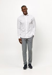 Witte lange mouw overhemd met knoopsluiting, gecombineerd met lichtgrijze broeken en donkere sneakers. Het overhemd heeft een gladde textuur.