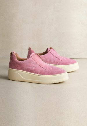 Pink suede slip-on shoes with a cream rubber sole and minimalistic design. Features stitching details and pull tabs on the heel.