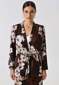 Giacca in stile kimono floreale in satin marrone scuro con grandi fiori chiari, maniche lunghe e cintura annodata in vita.