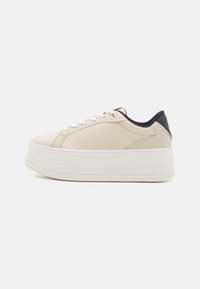 Beige syntetické tenisky s texturovaným svrškem, bílou platformovou podrážkou, námořnickými akcenty na patě a zlatými oky na šňůrky.