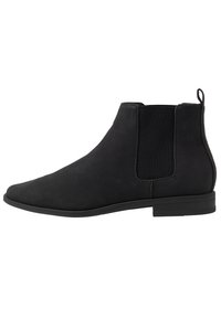 Botas Chelsea de ante negro con paneles laterales elásticos y una forma suave. Cuentan con una suela de goma baja y una asa en la parte trasera.