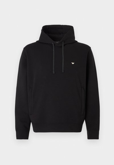 Melnā kapuce no mīksta auduma ar aukliņu kapuci, ķengura kabatu un mazu zelta logo uz krūtīm.