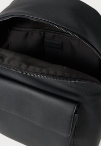 Fekete hátizsák texturált külsővel, cipzáras záródással és elülső zsebbel. Belseje fekete anyaggal bélelt a tartósság érdekében.