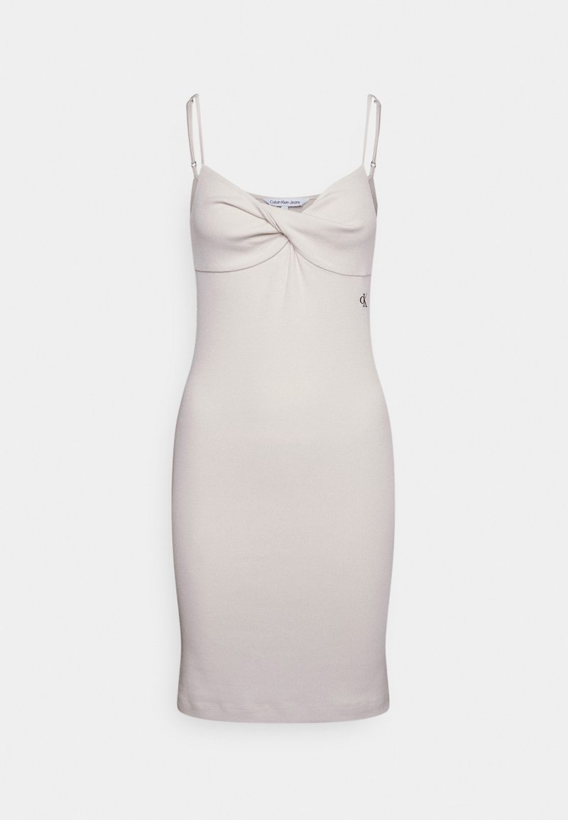 Vestido bodycon beige claro con tirantes finos, que presenta un detalle frontal retorcido y un sutil logo de Calvin Klein bordado en la cadera. Textura suave.