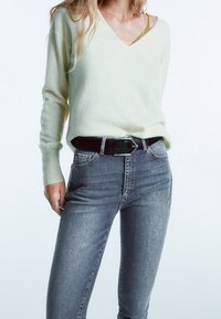 Lichtgroene v-hals sweater van zacht materiaal, gecombineerd met hoge, donkere skinny jeans en een zwarte riem met een zilveren gesp.
