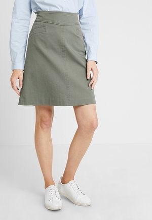 Jupe en coton vert olive avec une coupe droite, taille haute et deux poches avant, associée à des baskets blanches et une chemise bleu clair.